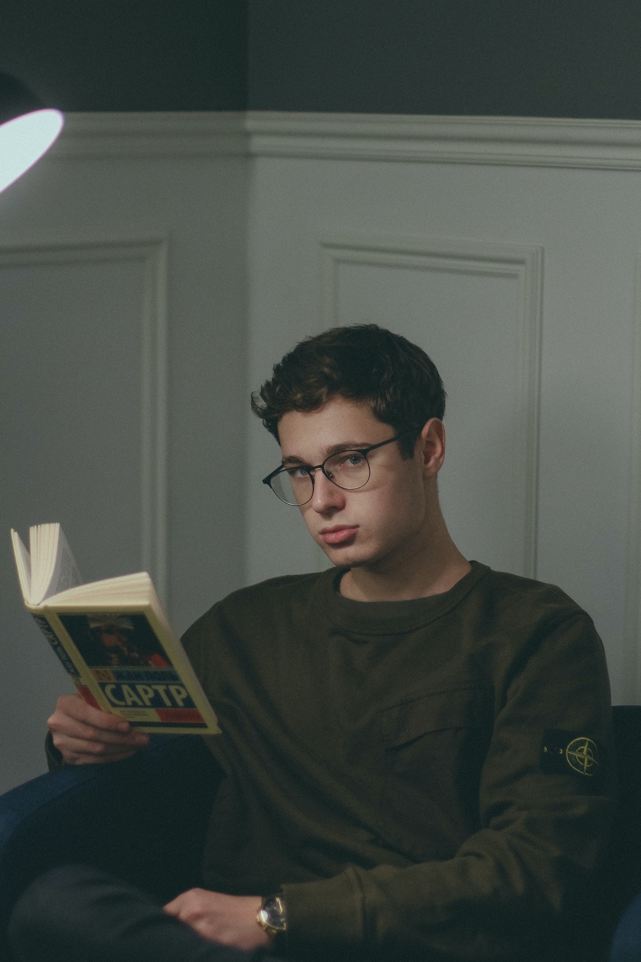 a man sitting, holding a book and glancing forward